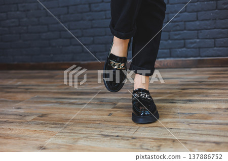 Close-up female legs in black trousers and leather black shoes. Women's shoes in patent leather with a metal buckle. New spring-summer collection of women's leather shoes 2022 Close-up female legs in black trousers and leather black shoes. Women's shoes in patent leather with a metal buckle. New spring-summer collection of women's leather shoes 2022 137886752