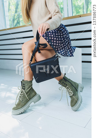 Fashionable leather boots on a woman's leg, close-up, fashionable. Leather bag in female hands. Fashionable leather boots on a woman's leg, close-up, fashionable. Leather bag in female hands. 137886773