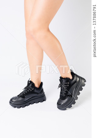 Fashionable black sneakers on the legs of a woman in the studio on a white background. Legs of a young girl with beautiful trendy shoes Fashionable black sneakers on the legs of a woman in the studio on a white background. Legs of a young girl with beautiful trendy shoes 137886791