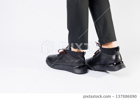 Stylish leather black short men's autumn sneakers on a white background on men's legs. Sneakers winter collection 2022. Stylish leather black short men's autumn sneakers on a white background on men's legs. Sneakers winter collection 2022. 137886890