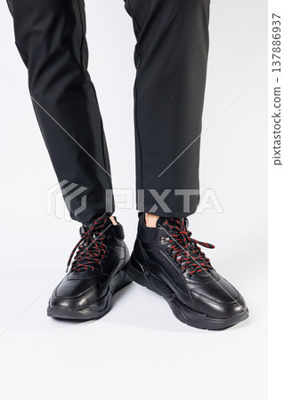 Stylish leather black short men's autumn sneakers on a white background on men's legs. Sneakers winter collection 2022. 137886937