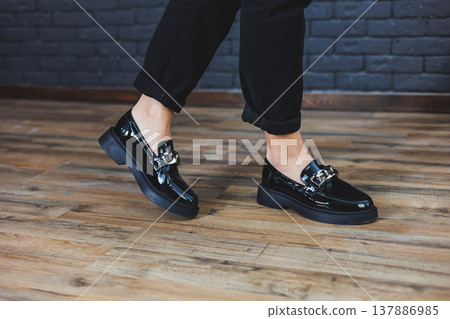 Close-up female legs in black trousers and leather black shoes. Women's shoes in patent leather with a metal buckle. New spring-summer collection of women's leather shoes 2022 Close-up female legs in black trousers and leather black shoes. Women's shoes in patent leather with a metal buckle. New spring-summer collection of women's leather shoes 2022 137886985