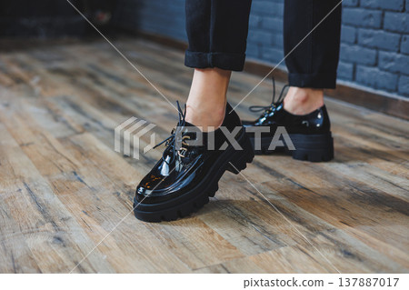 Beautiful woman with legs in fashionable clothes, stylish leather black patent leather lace-up shoes close-up. Women's image in spring style 137887017