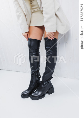 Black women's stocking boots made of genuine leather are worn on women's legs. New collection of women's boots 2022. Winter shoes Black women's stocking boots made of genuine leather are worn on women's legs. New collection of women's boots 2022. Winter shoes 137887024