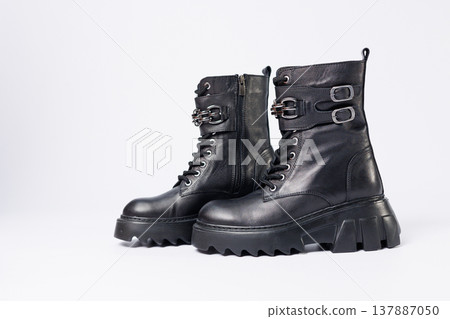 Women's shoes on a white background. Close-up of women's black leather boots with buckles on a white background. Shoes for the city. Concept for 2022 fashion, design and footwear. Women's shoes on a white background. Close-up of women's black leather boots with buckles on a white background. Shoes for the city. Concept for 2022 fashion, design and footwear. 137887050