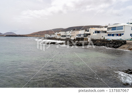 A coastal view of Punta Mujeres in Lanzarote, featuring white buildings and serene ocean water under a cloudy sky. A coastal view of Punta Mujeres in Lanzarote, featuring white buildings and serene ocean water under a cloudy sky. 137887067