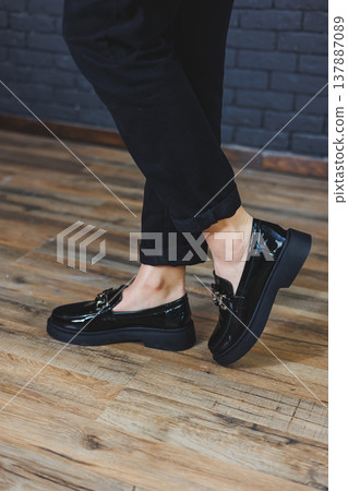 Close-up female legs in black trousers and leather black shoes. Women's shoes in patent leather with a metal buckle. New spring-summer collection of women's leather shoes 2022 137887089