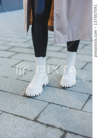 A cute young woman in a beige raincoat and autumn leather boots walks down the street. Autumn warm image. Women's fashion A cute young woman in a beige raincoat and autumn leather boots walks down the street. Autumn warm image. Women's fashion 137887091