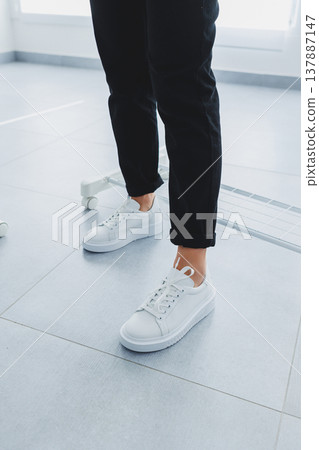 Women's legs in black trousers and white leather sneakers. Modern casual style. New shoe collection Women's legs in black trousers and white leather sneakers. Modern casual style. New shoe collection 137887147