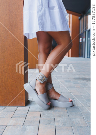 Female slender legs in white summer sandals. Women's leather shoes Female slender legs in white summer sandals. Women's leather shoes 137887158