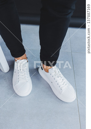 A man in white leather casual sneakers, summer men's sneakers. Man in black jeans A man in white leather casual sneakers, summer men's sneakers. Man in black jeans 137887169