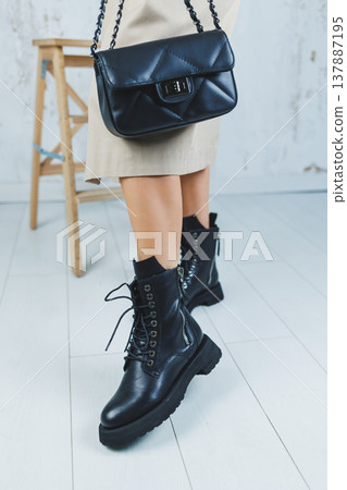 Close-up of female legs in black leather lace-up shoes. Black leather handbag in female hands. New autumn collection of women's leather shoes 2022 137887195
