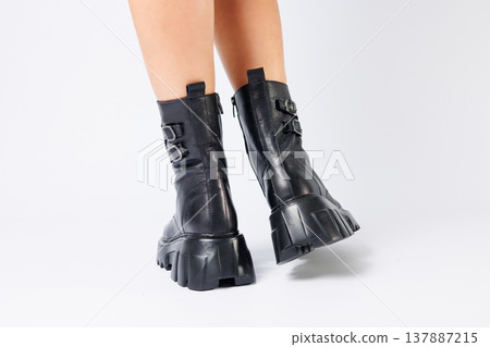 Legs of a woman in black leather boots from a new collection on a white background, legs of a girl in fashionable leather boots spring 2022. Legs of a woman in black leather boots from a new collection on a white background, legs of a girl in fashionable leather boots spring 2022. 137887215