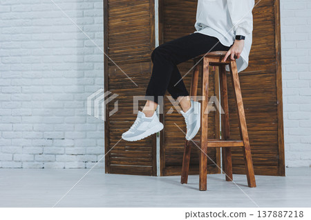 Close-up of female legs in black jeans in stylish leather white sneakers. Fashionable woman in new sneakers. Modern seasonal collection of stylish sneakers. Women's fashion. 137887218