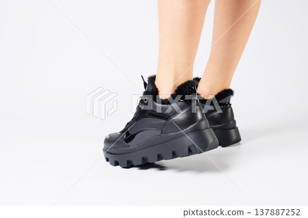 Fashionable black sneakers on the legs of a woman in the studio on a white background. Legs of a young girl with beautiful trendy shoes Fashionable black sneakers on the legs of a woman in the studio on a white background. Legs of a young girl with beautiful trendy shoes 137887252