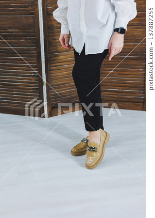 Close-up of female legs in black jeans in stylish leather beige shoes. Fashionable woman in new loafers. Modern seasonal collection of stylish shoes. Women's fashion. 137887255