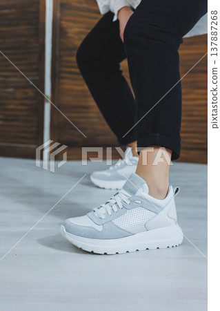 Beautiful women's shoes with legs, leather white sneakers, in the interior of a room or office, shoes for a woman, black trousers and white sneakers, casual and modern style, modern and trendy Beautiful women's shoes with legs, leather white sneakers, in the interior of a room or office, shoes for a woman, black trousers and white sneakers, casual and modern style, modern and trendy 137887268