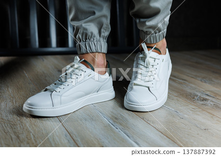 Casual white sneakers for men. Male legs in white leather summer shoes. Comfortable men's white sneakers with laces. Casual white sneakers for men. Male legs in white leather summer shoes. Comfortable men's white sneakers with laces. 137887392