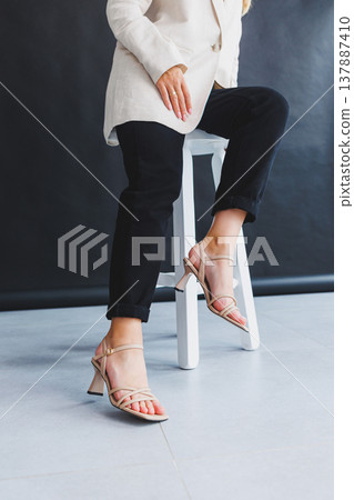 Women's legs close-up in summer brown flip-flops with heels. Summer collection of shoes for women made of genuine leather Women's legs close-up in summer brown flip-flops with heels. Summer collection of shoes for women made of genuine leather 137887410