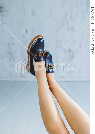 Female legs in black leather loafers. Autumn women's shoes without a heel Female legs in black leather loafers. Autumn women's shoes without a heel 137887413