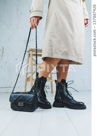 Close-up of female legs in black leather lace-up shoes. Black leather handbag in female hands. New autumn collection of women's leather shoes 2022 137887426