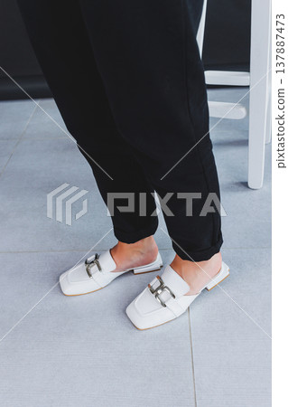 White female leather slippers close-up on female legs. New collection of women's summer leather shoes. White female leather slippers close-up on female legs. New collection of women's summer leather shoes. 137887473