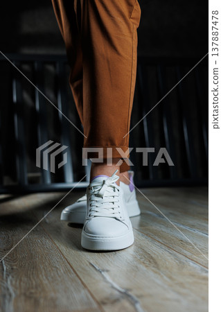 Comfortable women's sneakers on a flat sole with laces. Close-up of female legs in white perforated leather sneakers. Women's summer sneakers. Collection of women's leather shoes Comfortable women's sneakers on a flat sole with laces. Close-up of female legs in white perforated leather sneakers. Women's summer sneakers. Collection of women's leather shoes 137887478