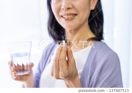 Senior woman taking medicine by the window Senior woman taking medicine by the window 137887513