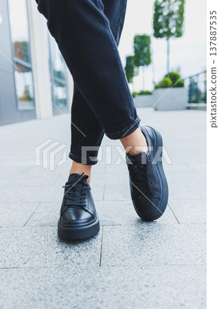 Female legs in black jeans and black lace-up shoes. Black leather shoes close-up Female legs in black jeans and black lace-up shoes. Black leather shoes close-up 137887535