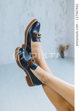Female legs in black leather loafers. Autumn women's shoes without a heel Female legs in black leather loafers. Autumn women's shoes without a heel 137887602