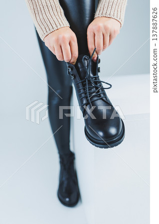 Female legs in leather black autumn boots. A fashion girl stands in a store and measures shoes. Female legs in leather black autumn boots. A fashion girl stands in a store and measures shoes. 137887626