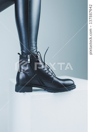 Female legs in leather black autumn boots. A fashion girl stands in a store and measures shoes. Female legs in leather black autumn boots. A fashion girl stands in a store and measures shoes. 137887642