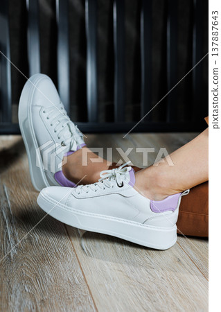 White leather sneakers on women's legs. Women's legs in comfortable casual sneakers 137887643