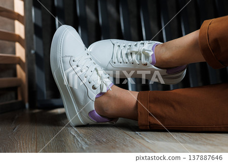 Comfortable female legs in white sneakers with flat soles. Close-up of female legs in leather sneakers. Women's summer sneakers. Collection of women's leather shoes 137887646