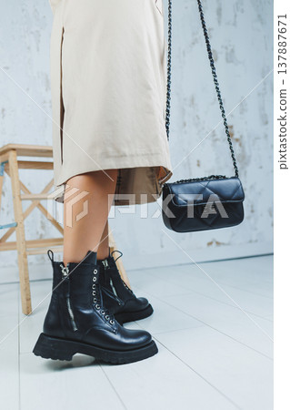 Close-up of female legs in black leather lace-up shoes. Black leather handbag in female hands. New autumn collection of women's leather shoes 2022 Close-up of female legs in black leather lace-up shoes. Black leather handbag in female hands. New autumn collection of women's leather shoes 2022 137887671