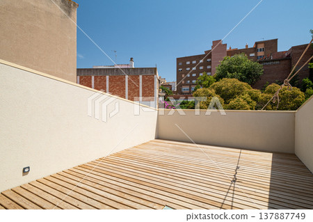 A modern terrace with wooden flooring and a clear blue sky. Surrounding buildings and greenery are visible in the background. A modern terrace with wooden flooring and a clear blue sky. Surrounding buildings and greenery are visible in the background. 137887749