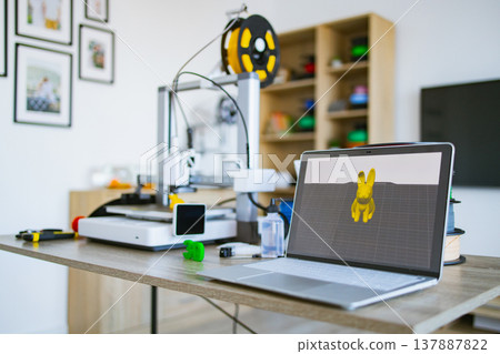 A modern 3D printer is connected to a laptop displaying a 3D model, ready for creation A modern 3D printer is connected to a laptop displaying a 3D model, ready for creation 137887822