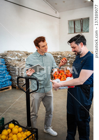 Warehouse workers discussing produce quality holding fresh tomatoes Warehouse workers discussing produce quality holding fresh tomatoes 137889077
