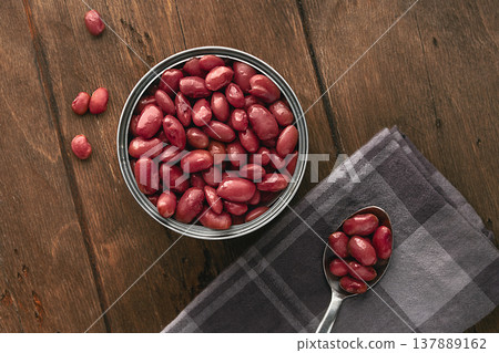 Red canned kidney beans served in a minimalist rustic style on a wooden table in a tin can top view Flat Lay. An open tin can filled to the brim with glossy red beans. Several beans are placed Red canned kidney beans served in a minimalist rustic style on a wooden table in a tin can top view Flat Lay. An open tin can filled to the brim with glossy red beans. Several beans are placed 137889162