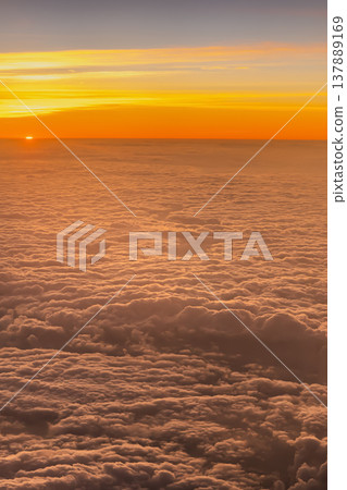 Sun sinks below the horizon while clouds stretch across the sky, creating an orange glow in the background. The view is captured from the window of an airplane flying high. High quality photo Sun sinks below the horizon while clouds stretch across the sky, creating an orange glow in the background. The view is captured from the window of an airplane flying high. High quality photo 137889169