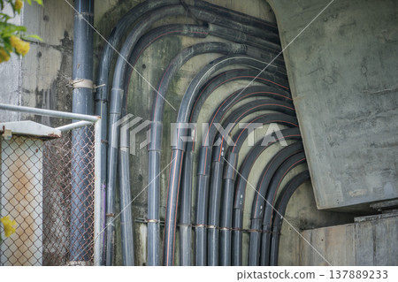 Laying of powerful power cables laid in HDPE protective pipes along a concrete structure concrete bridge or overpass engineering structure fragment. Safe transmission of electricity to high-voltage or Laying of powerful power cables laid in HDPE protective pipes along a concrete structure concrete bridge or overpass engineering structure fragment. Safe transmission of electricity to high-voltage or 137889233