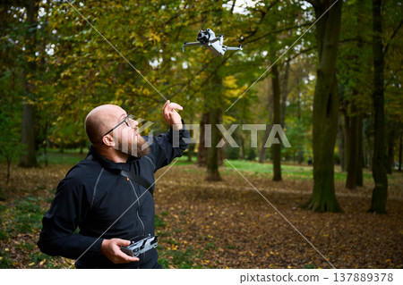 Man playing with drone in autumn park, flying quadcopter with remote controller, outdoor hobby and leisure activity, modern technology and recreation concept 137889378