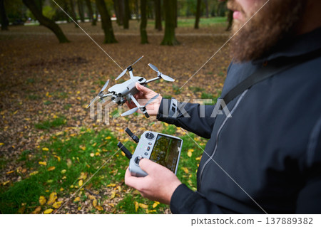 Man holds drone and checks controller before flight. Bearded man preparing quadcopter in a park, setting up equipment for aerial photography, concept of modern technology and hobby Man holds drone and checks controller before flight. Bearded man preparing quadcopter in a park, setting up equipment for aerial photography, concept of modern technology and hobby 137889382