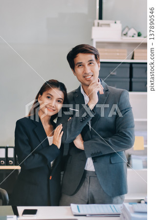 Portrait of a happy Asian business couple standing together. Young professional man and woman smiling in studio. Corporate teamwork concept Portrait of a happy Asian business couple standing together. Young professional man and woman smiling in studio. Corporate teamwork concept 137890546