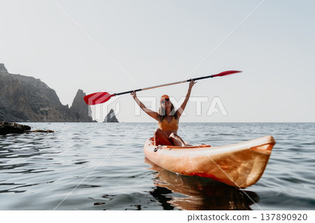 Woman Kayak Paddle Ocean: Woman paddles a kayak in a calm ocean with mountains in the background. Woman Kayak Paddle Ocean: Woman paddles a kayak in a calm ocean with mountains in the background. 137890920