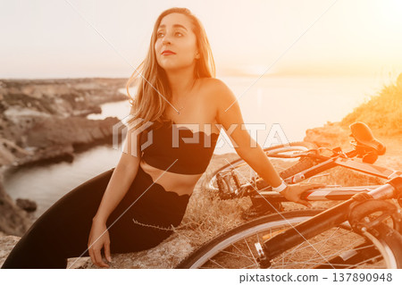 Woman bicycle sunset relaxing on a rocky cliff edge by the sea during a golden hour cycling break 137890948