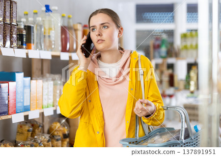 Young woman choosing groceries while talking on phone Young woman choosing groceries while talking on phone 137891951