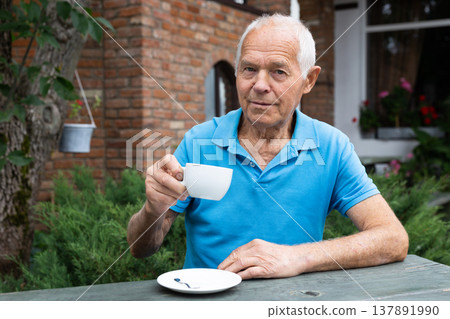 Elderly man holding cup of tea while relaxing on terrace of street cafe Elderly man holding cup of tea while relaxing on terrace of street cafe 137891990