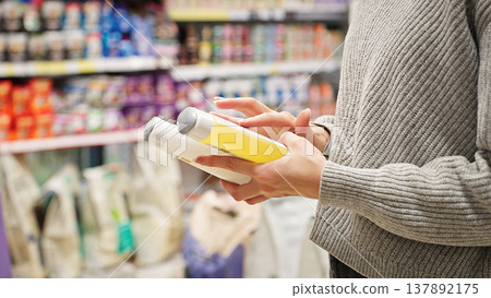 Woman shopper reading the label and ingredients of pet shampoo for her cat or dog, illustrating the concept of careful grooming product selection. Woman shopper reading the label and ingredients of pet shampoo for her cat or dog, illustrating the concept of careful grooming product selection. 137892175