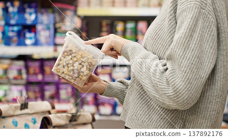 Woman choosing dry dog food in a pet store, reading the label and ingredients, illustrating responsible pet owner care and selection. Woman choosing dry dog food in a pet store, reading the label and ingredients, illustrating responsible pet owner care and selection. 137892176